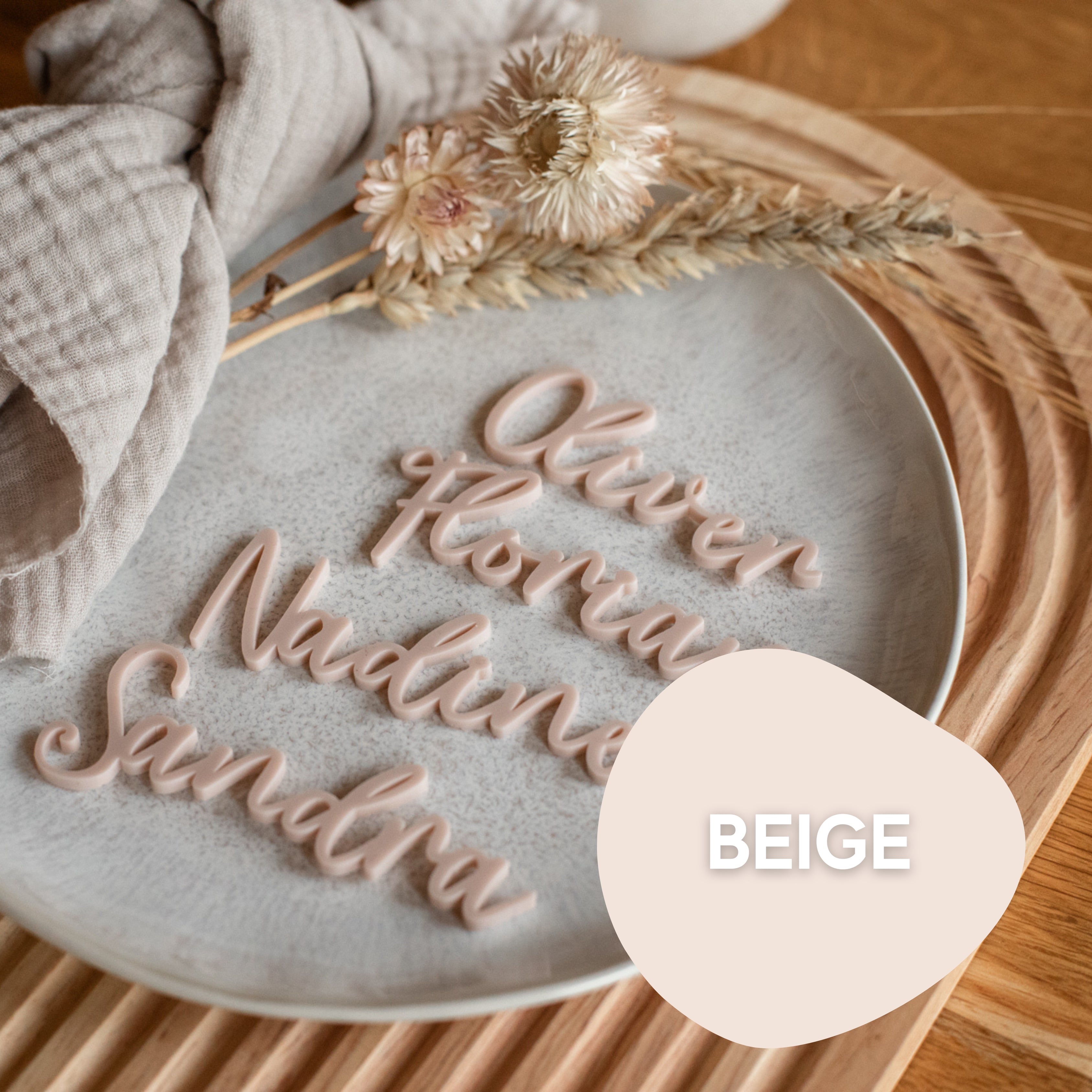 Die beigefarbenen „Namensschilder Hochzeit“ aus Stoff von laserhelden, präsentiert auf einem Teller mit Trockenblumen und auf einem Holztablett neben gefalteten Tischdecken platziert, verleihen Ihrer Hochzeitstafel eine elegante Note und verleihen personalisierten Tischkarten mühelos Charme.