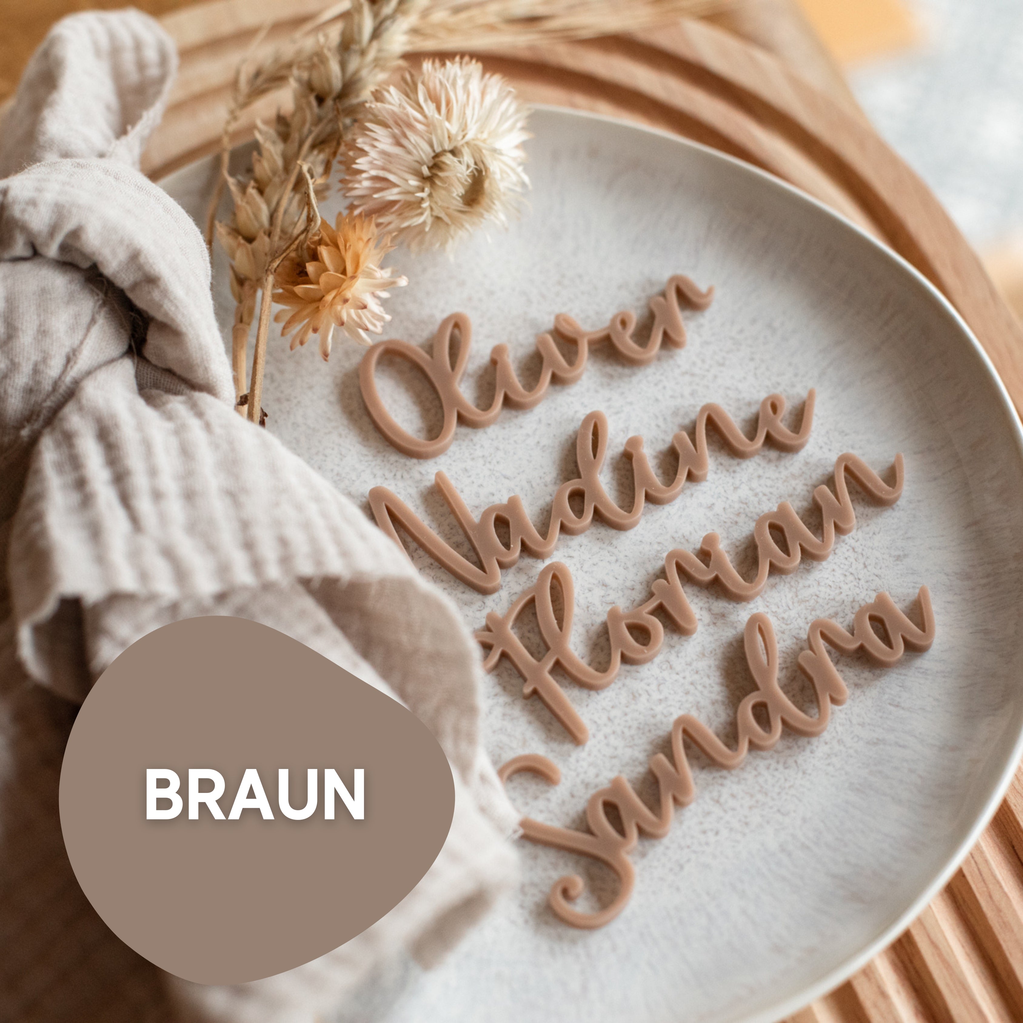 Ein Teller mit Namensschildern Hochzeit von laserhelden mit personalisierten Namenskarten aus Acryl in Schreibschrift: Oliver, Nadine, Florian, Sandra. Mit Trockenblumen und einem Tuch dekoriert. Ideal als Tischkarten für Hochzeit.