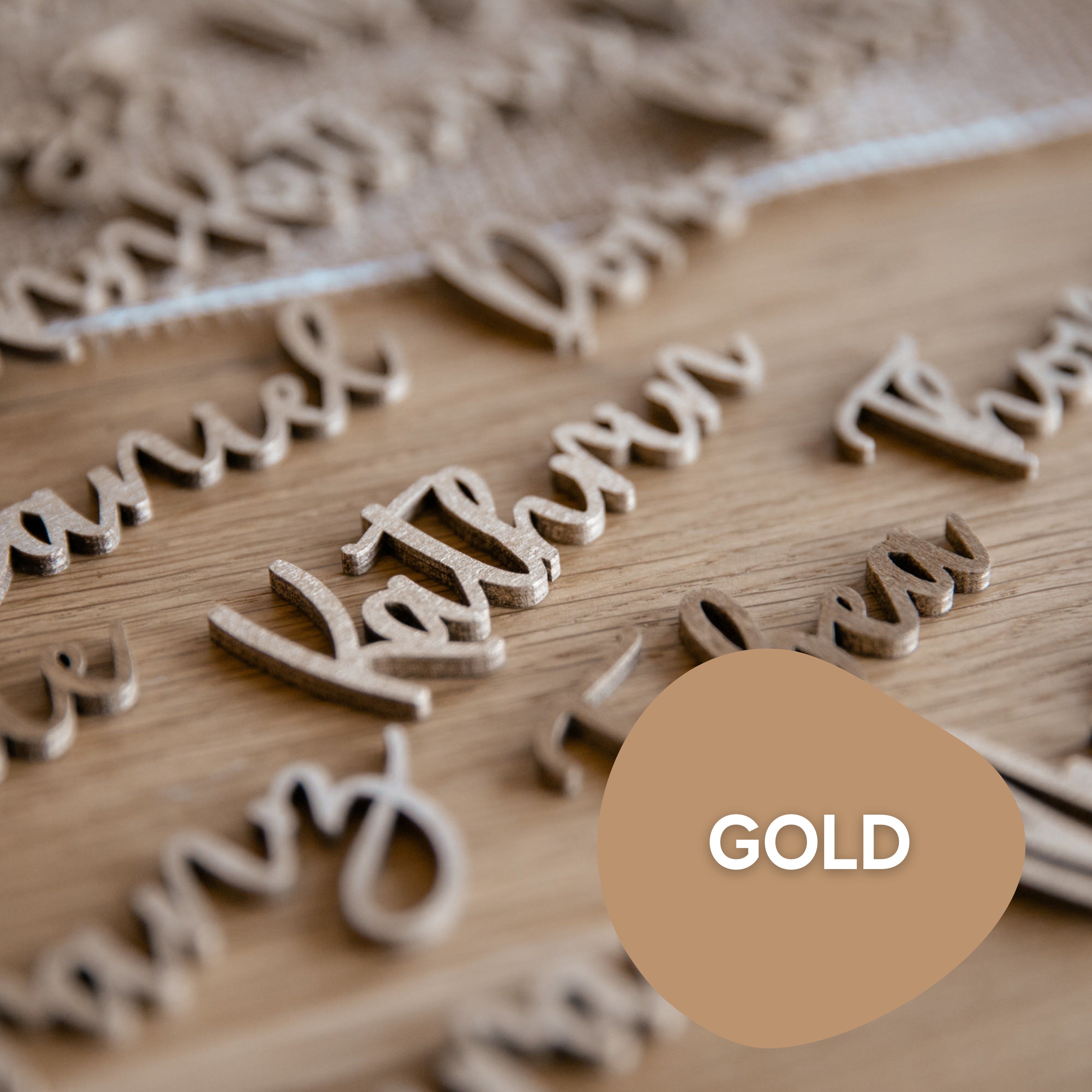 Laserheldens Hochzeit Tischkarten Schriftzug aus Holz in Gold, Silber oder Kupfer schmückt elegant einen Tisch und bietet handgefertigte Tischdekoration. Ein goldenes Farbmuster mit der Aufschrift „Gold“ unterstreicht seine Raffinesse.