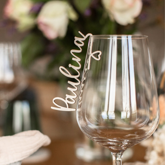 Der „Glasmarkierer mit Namen aus Holz“ von Laserhelden ruht elegant auf dem Tisch, mit dem ausgeschnittenen Schriftzug „Paulina“, verziert mit verschwommenen Blumen – eine ideale Hochzeitsdekoration, die Ihre Liebe zum Detail zeigt.