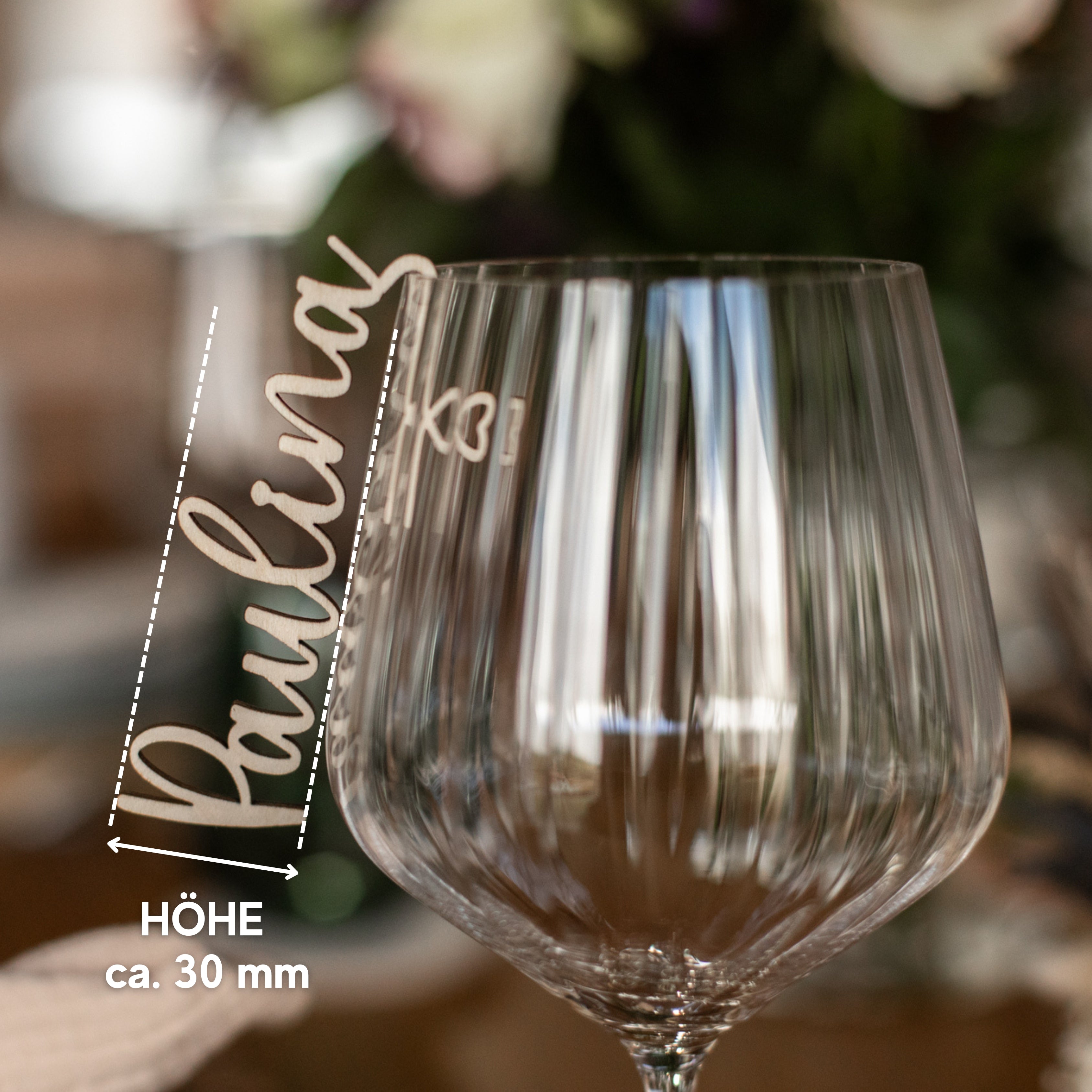 Nahaufnahme eines Weinglases mit der Gravur „Paulina“, ideal als Hochzeitsdekoration. Die dezente HÖHE von ca. 30 mm ist im unscharfen Hintergrund gut zu erkennen und eignet sich daher perfekt für eine individuelle Tischdekoration mit dem Glasmarkierer mit Namen aus Holz von laserhelden.