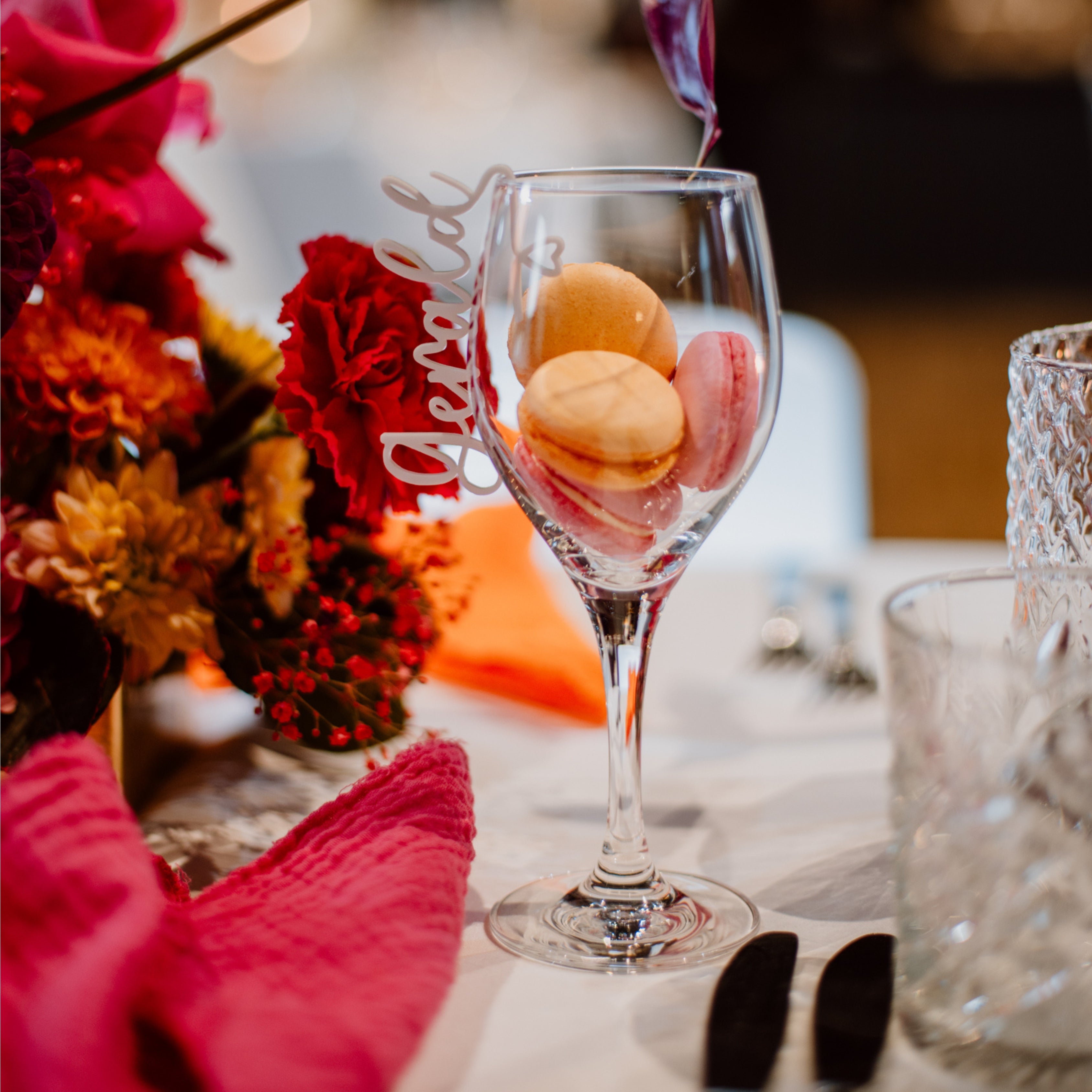 Macarons in einem Weinglas mit laserhelden Glasmarkierer personalisiert aus Acryl, gedeckt auf einem mit Blumen geschmückten Tisch und einer orangefarbenen Serviette.
