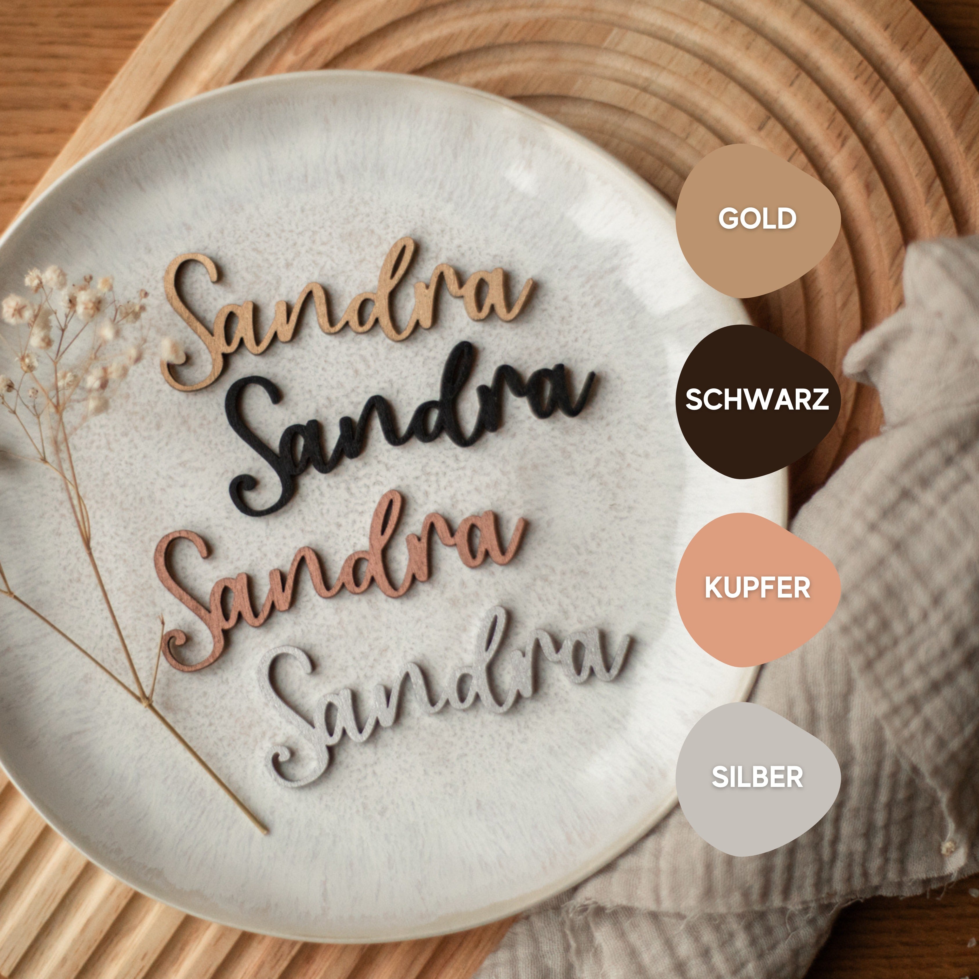 Fünf Holzfiguren „Sandra“ in Gold, Schwarz, Kupfer und Silber verzieren einen Teller mit farbigen Etiketten, Tischtuch und kleinen Blumen. Diese edlen handgefertigten Tischdekorationen von laserhelden eignen sich perfekt als Platzkarten für Hochzeiten.