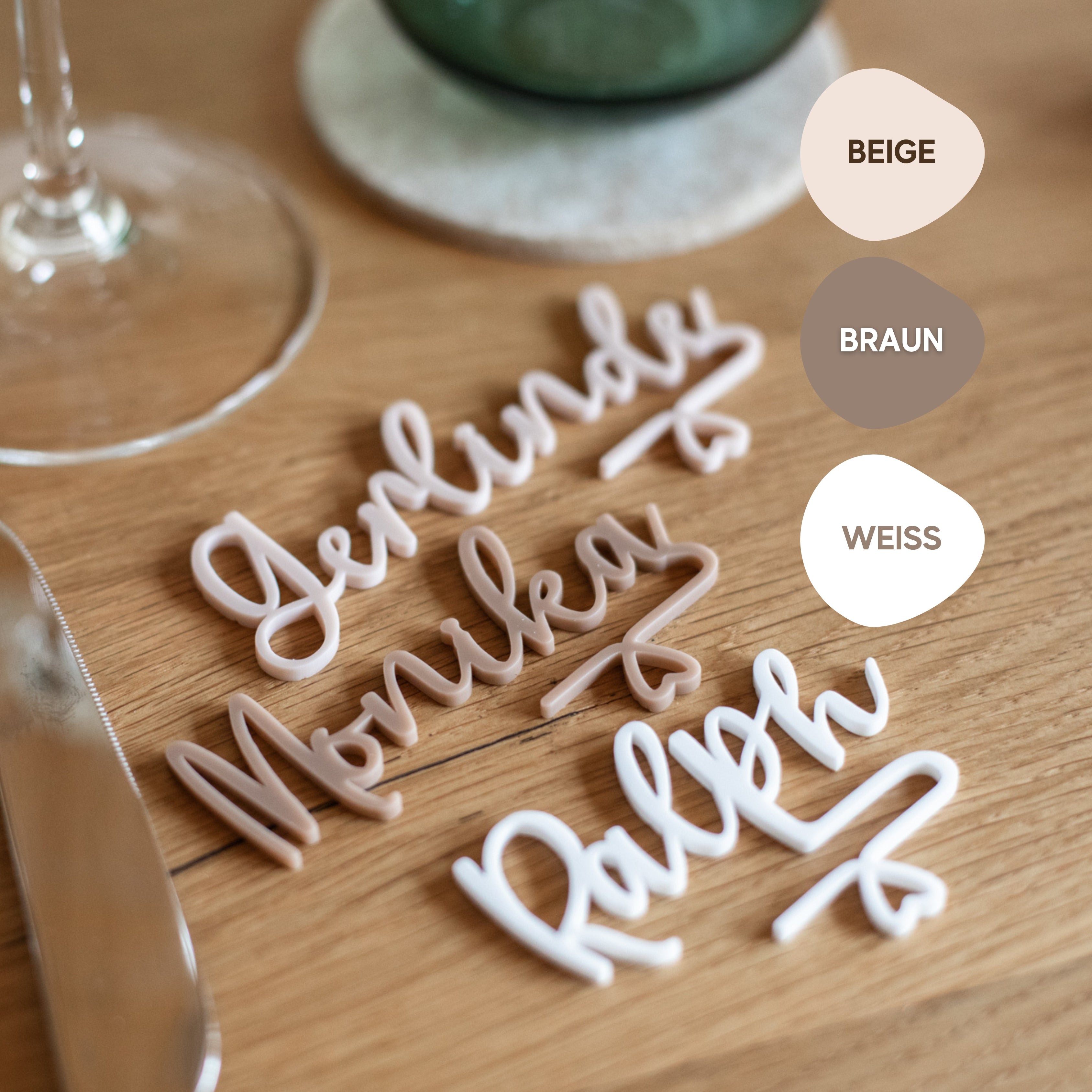 Auf einem Tisch sind kursive Namensschilder mit dem personalisierten Glasmarkierer aus Acryl von Laserhelden angebracht, daneben liegen Farbmuster mit den Beschriftungen Beige, Braun und Weiß – perfekt für eine Hochzeit.