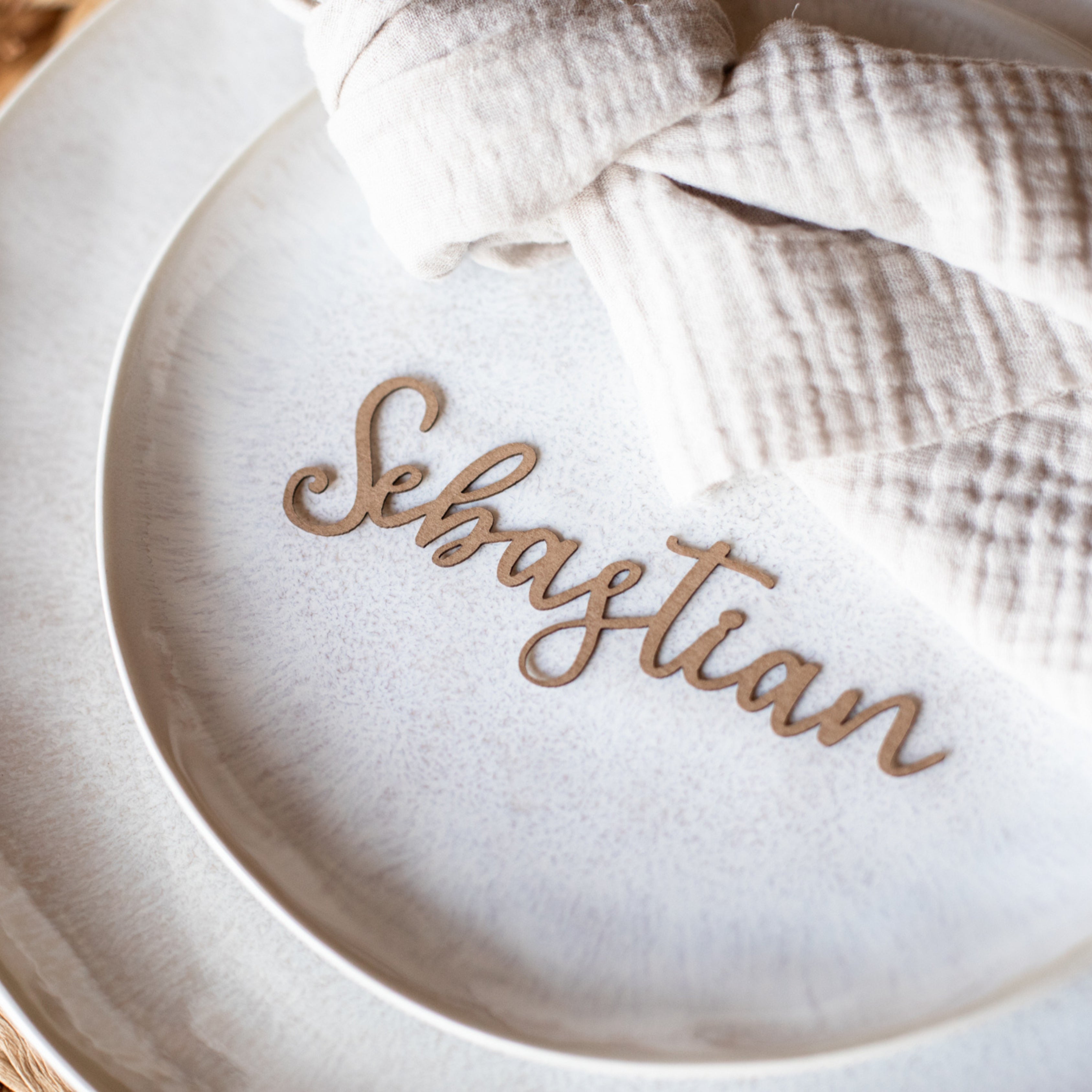 Ein personalisierter Kraftpapier-Teller „Sebastian“ von Laserhelden, gepaart mit einer beigen Stoffserviette, ist perfekt für ein Boho-Hochzeit-Thema und verleiht diesen Namensschild Hochzeit – Schriftzug aus Kraftpapier-Artikeln rustikalen Charme.