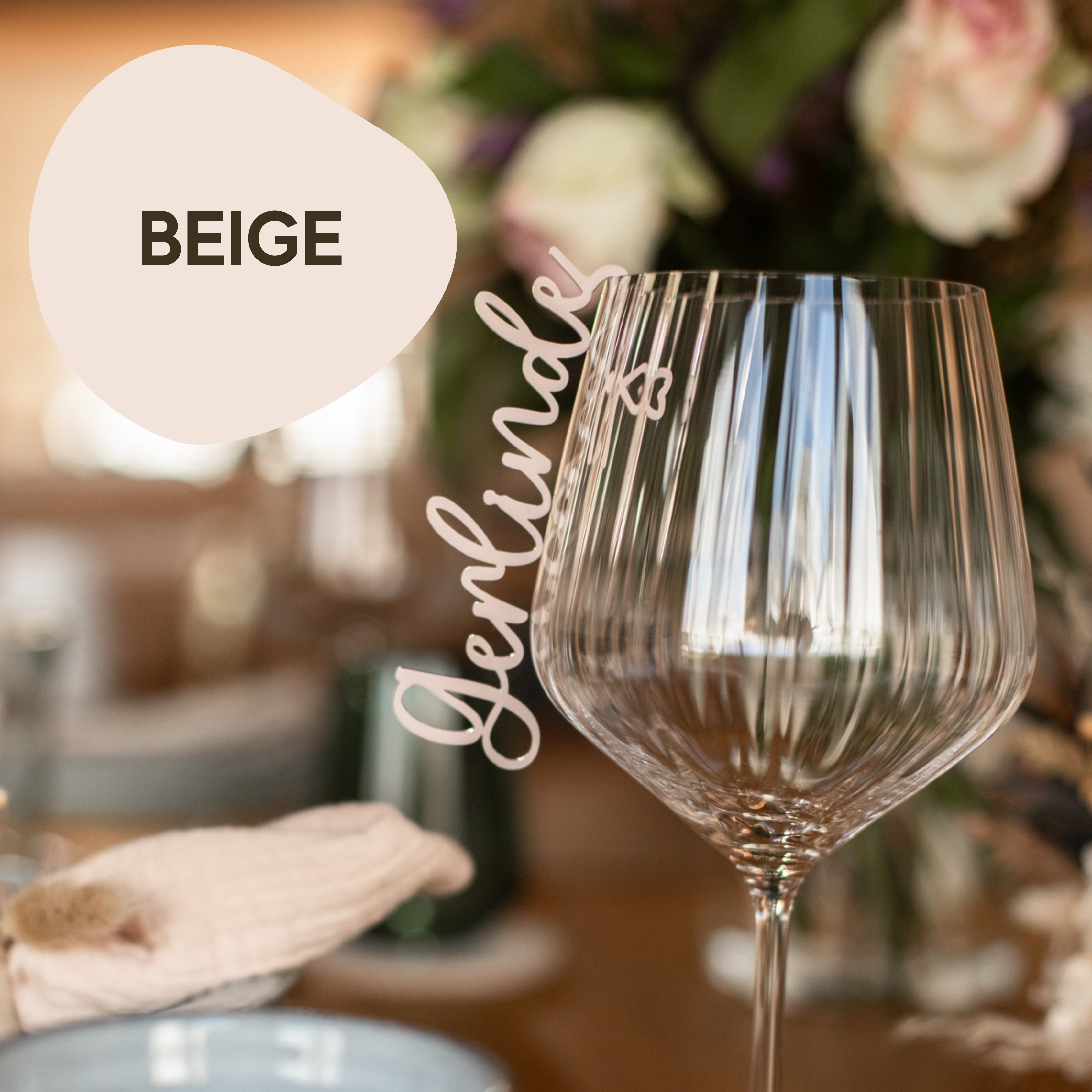 Eine Nahaufnahme eines leeren Weinglases auf einem gedeckten Tisch mit den Textüberlagerungen „Beige“ und „Jerlinde“. Das Glasmarkierer-Set aus Acryl von laserhelden verleiht jedem Anlass eine persönliche Note.