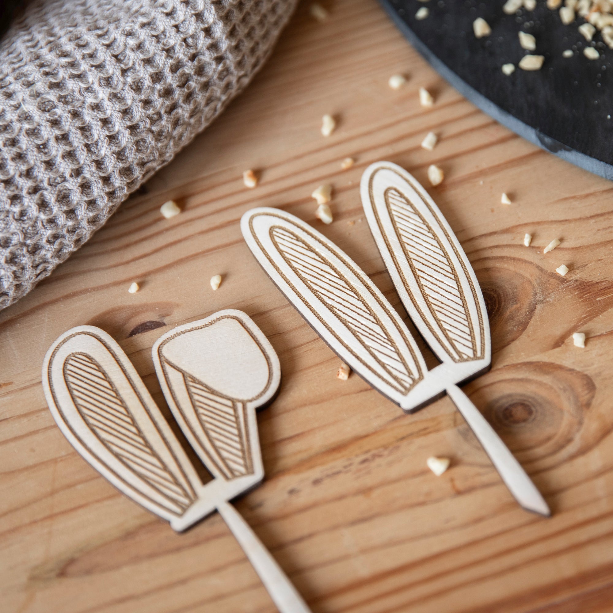 Laserheldens Cake-Topper/Muffinstecker in Hasenform mit aufwendigem Blättermuster liegen auf einem Holztisch, umgeben von verstreuten Krümeln.