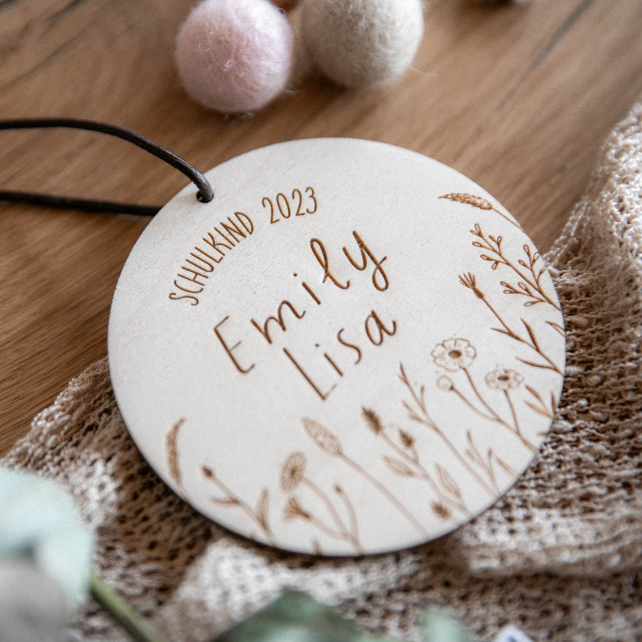 Der laserhelden Schultütenanhänger zur Einschulung aus Holz ist ein rundes Holzornament mit der Gravur „Schulkind 2023 Emily Lisa“ und verziert mit floralen Motiven, ideal als Schultüten-Accessoire.