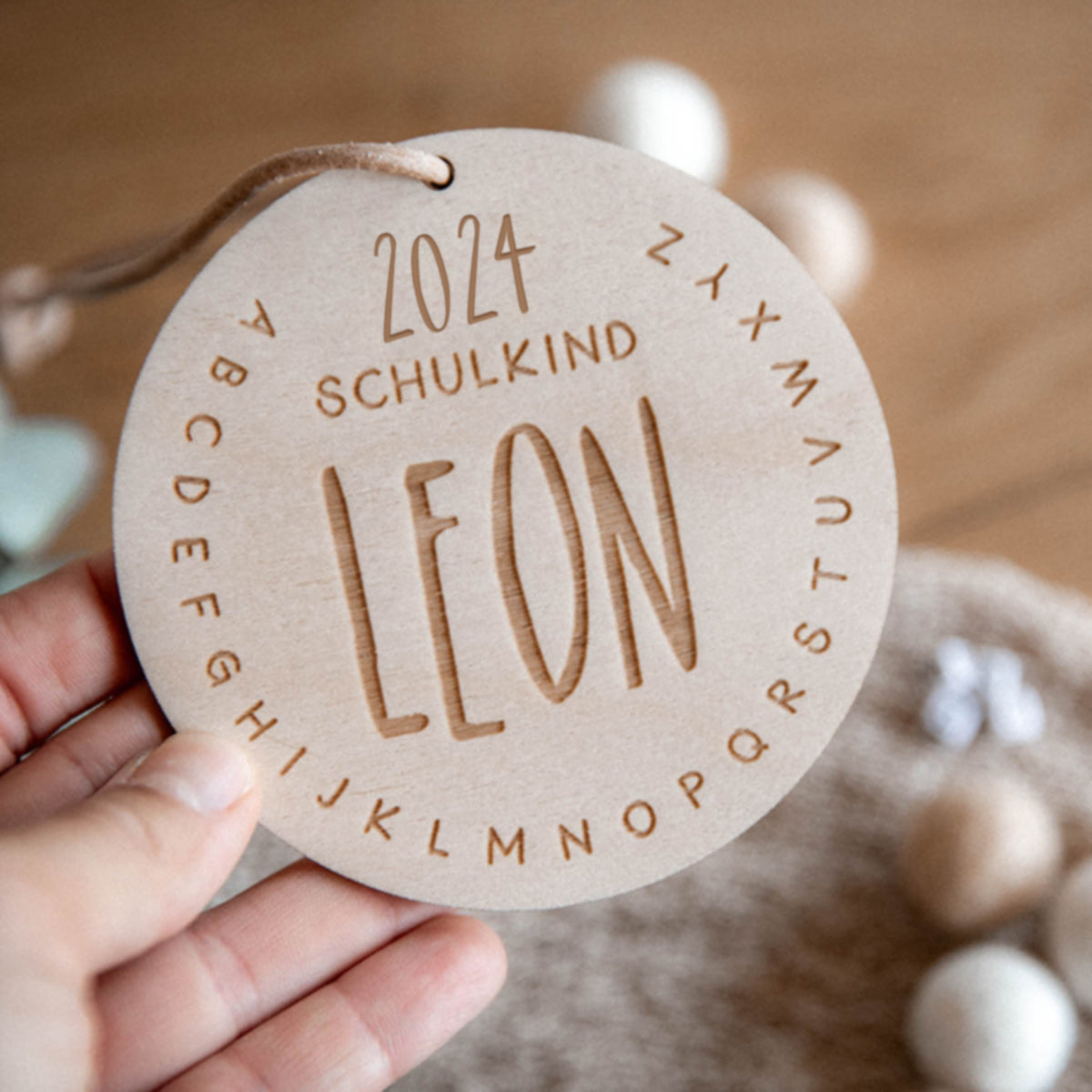 Ein laserhelden Schultütenanhänger zur Einschulung aus Holz, mit „Schulkind 2024“ und „Leon“ mit ABC-Motiv, zart in der Hand gehalten.