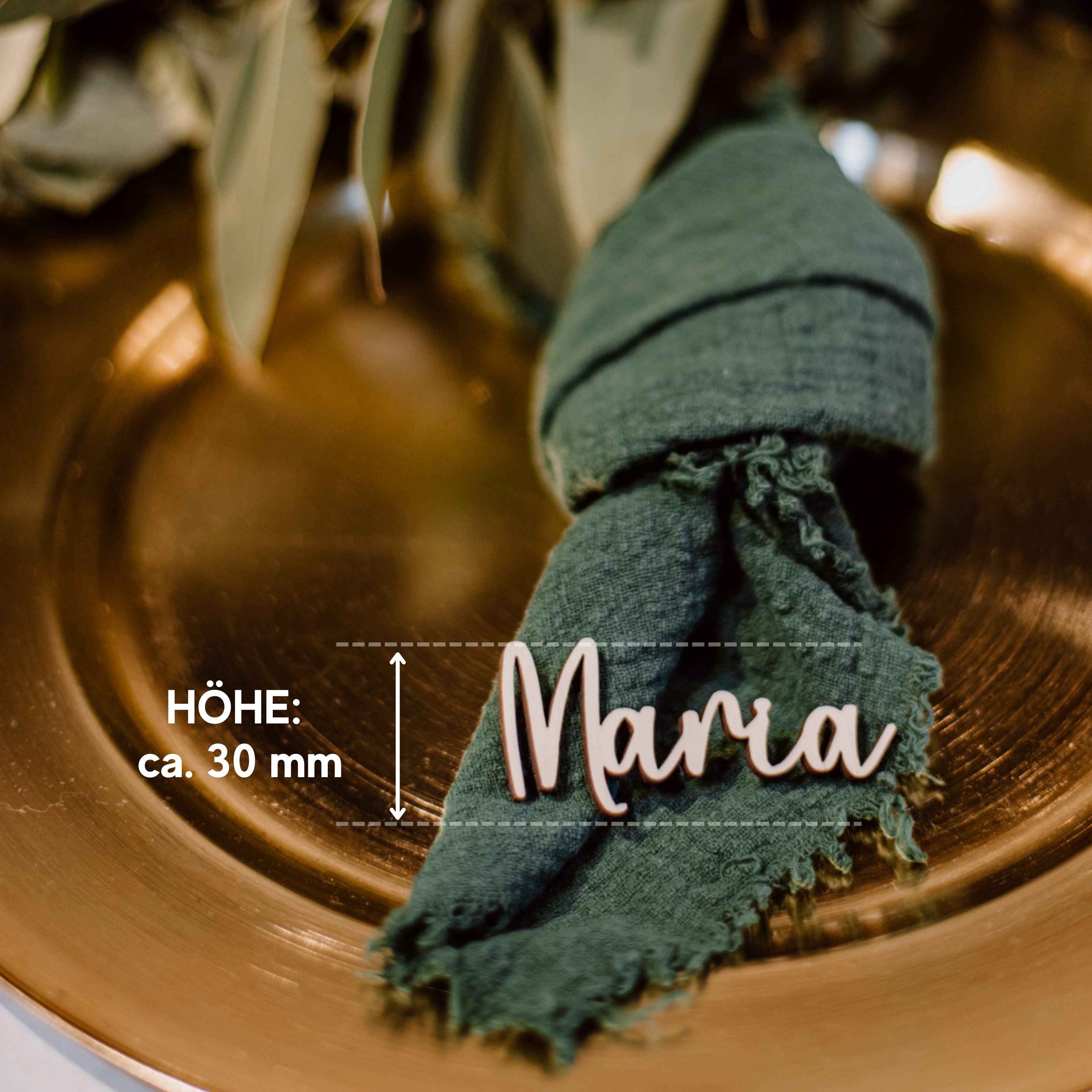 Auf einem goldenen Teller liegen eine grüne Serviette und die Namenskarte „Mara“ von Laserhelden mit der Aufschrift „Höhe: ca. 30 mm Text. Diese mit Blattdekor verzierten Tischkarten Hochzeit aus Holz sind handgefertigt und dienen als nachhaltiger Platzhalter, um Ihrer Umgebung eine umweltfreundliche Note zu verleihen.